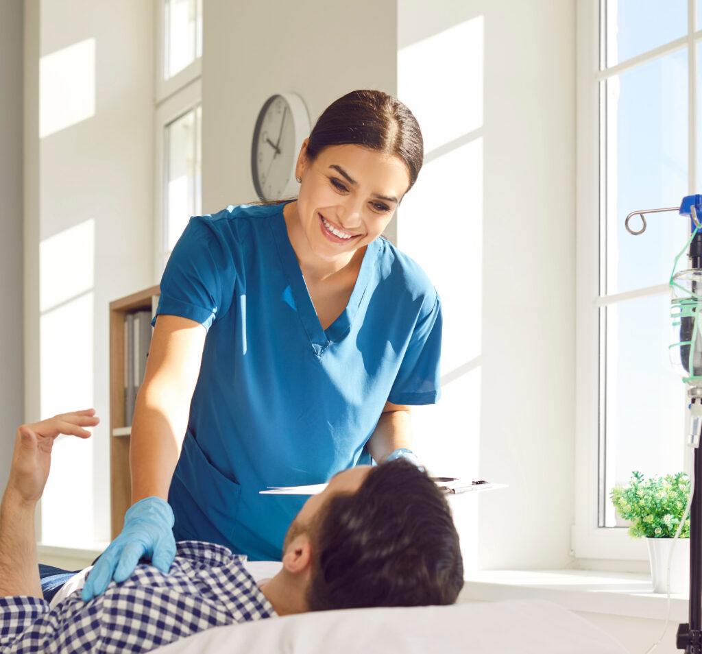 A Male Patient Lying Down at Home while a Female Nurse Administers a Vitamin IV Drip.