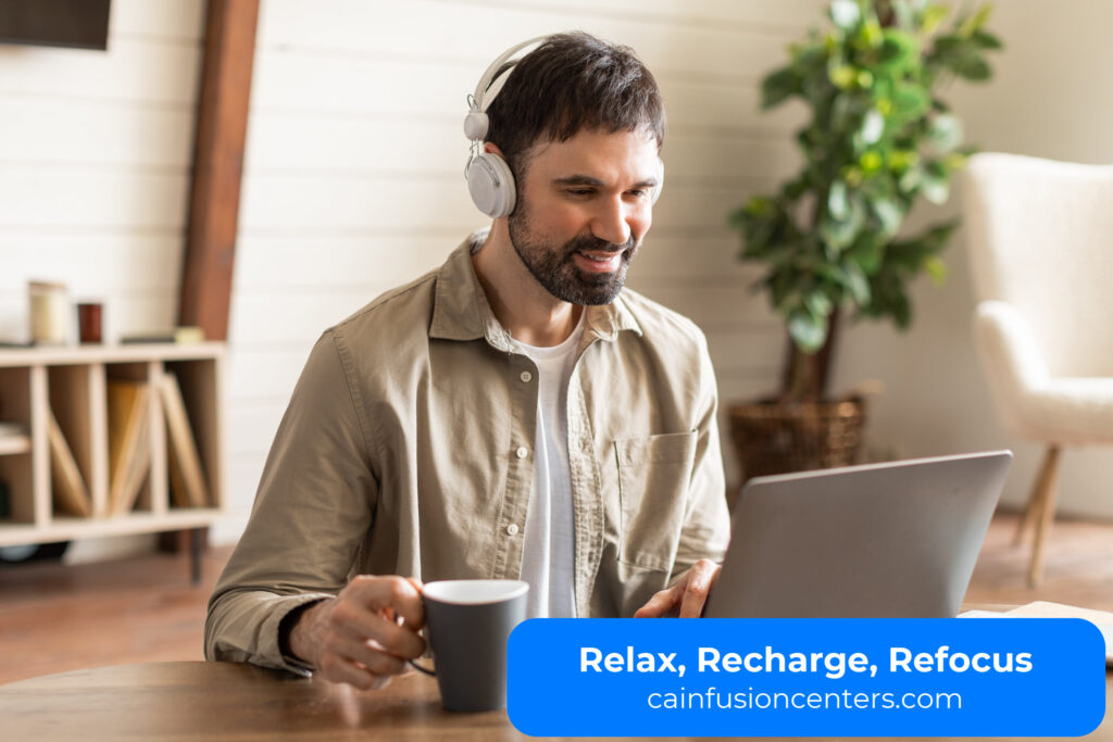 Man working comfortably on laptop with headphones and coffee, showing focus and calm after an IV therapy session.